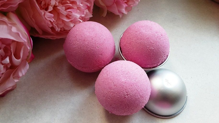 three pink bath fizzies scented in bubblegum placed on the table next to pink peonies