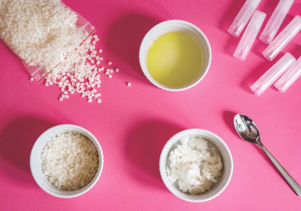 ingredients for making shea butter lip balm at home beeswax shea butter argan oil chamomile essential oil and lip balm tubes displayed on the table. ready for making a homemade shea butter lip balm recipe