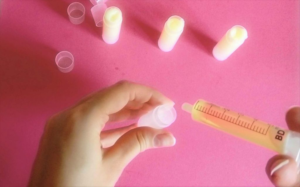 pouring homemade shea butter lip balm mixture into chapstick tubes pouring homemade lip balm mixture into chapstick tubes with a syringe. already filled lip balm tubes area standing on the table
