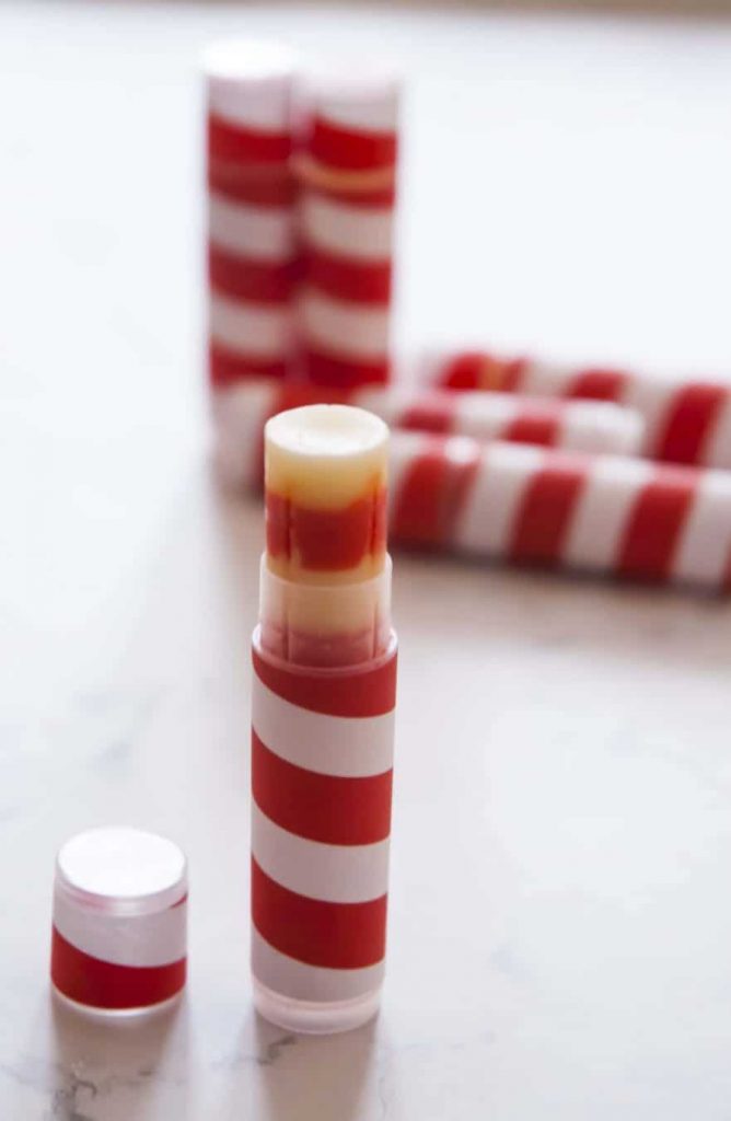 Six DIY candy cane scented lip balms on the table. All lip balms wrapped in red white stripe labels to resemble candy cane