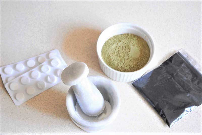 showing how to make charcoal mask. Displayed are ingredients neesary to make this homemade mask: french green clay, activated charcoal powder and aspirin. Showing how to grind aspirin tablets in mortar and pestle