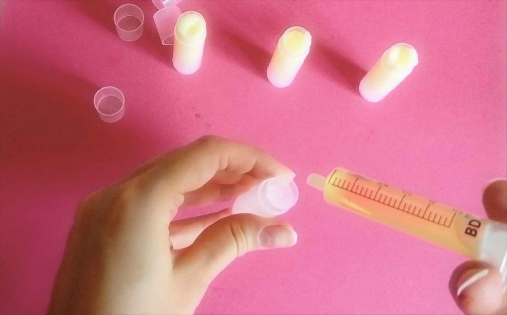 pouring homemade lip balm mixture into chapstick tubes with a syringe. already filled lip balm tubes area standing on the table