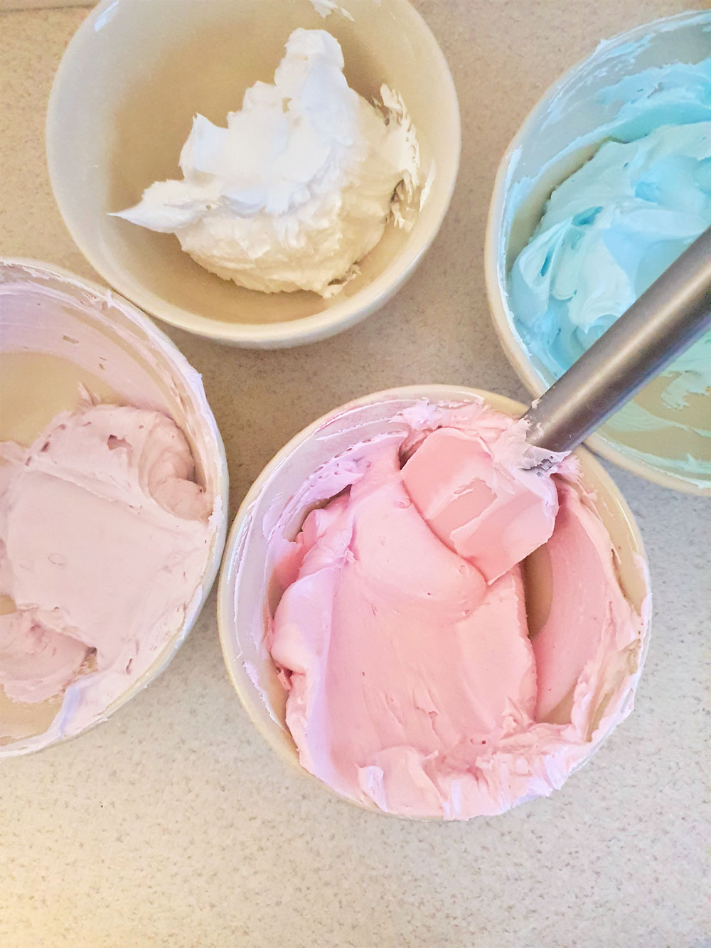 four bowls of whipped soap colored in pink, purple, blue and white
